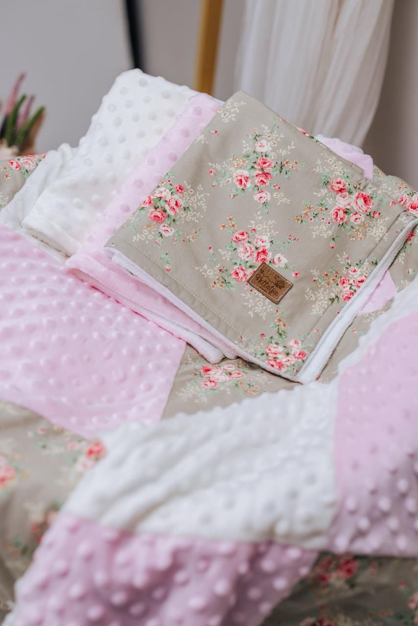 Soft pink and floral patterned baby bedding with delicate fabric textures layered together.