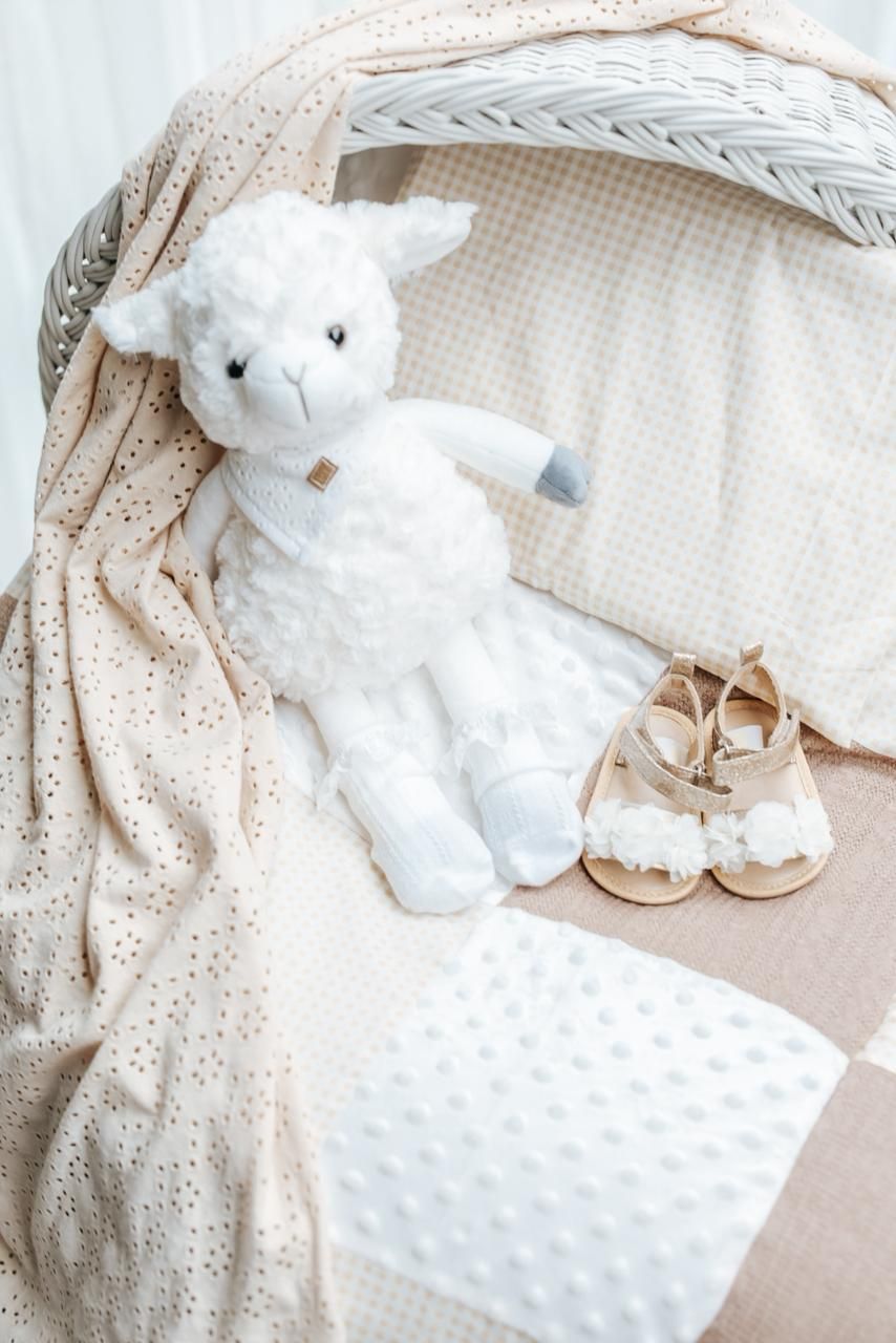 White stuffed teddy bear and blanket with delicate eyelet lace pattern on neutral beige background.