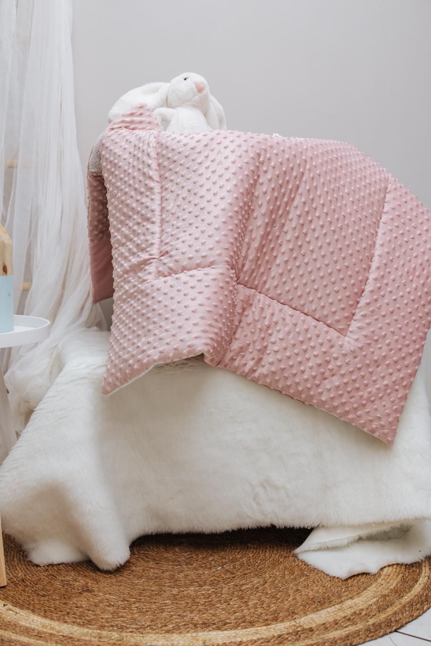 Pink quilted minky blanket with white faux fur trim displayed on a round woven jute rug.