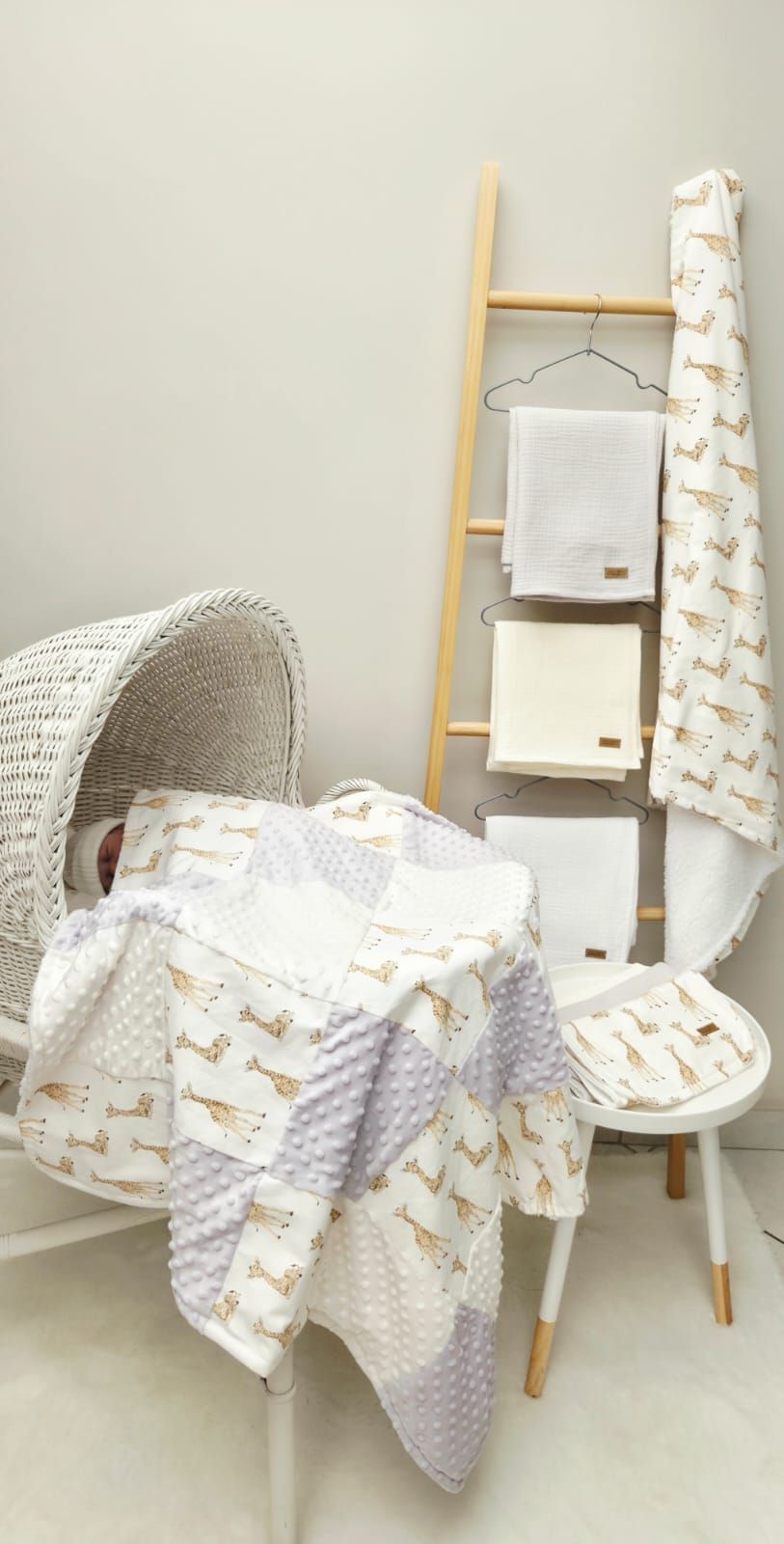 Cozy nursery corner with white and gold giraffe print blankets, ladder towel rack, and wicker chair.