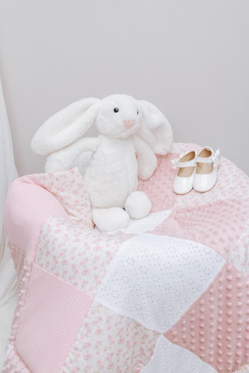 Delicate pink and white baby bedding with stuffed bunnies and small shoes.