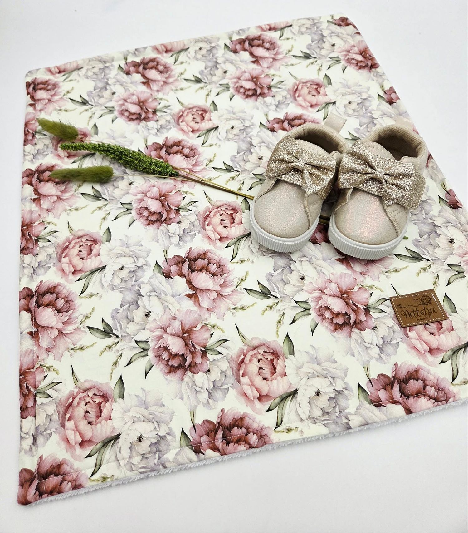 Vintage floral baby blanket with pink roses pattern and beige shoes arranged on white surface.