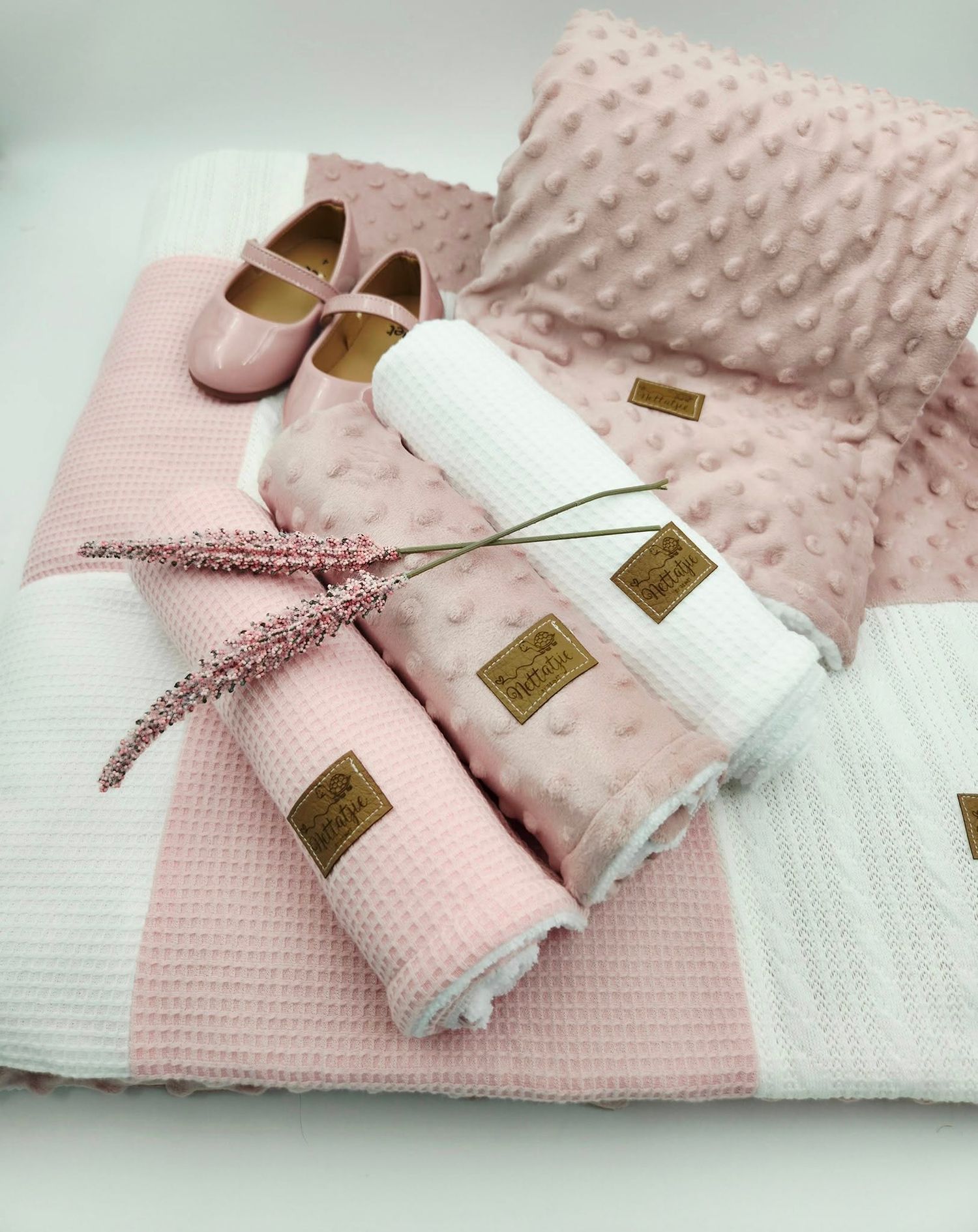 Pink minky dot blanket with white waffle trim and decorative bow displayed with baby shoes.