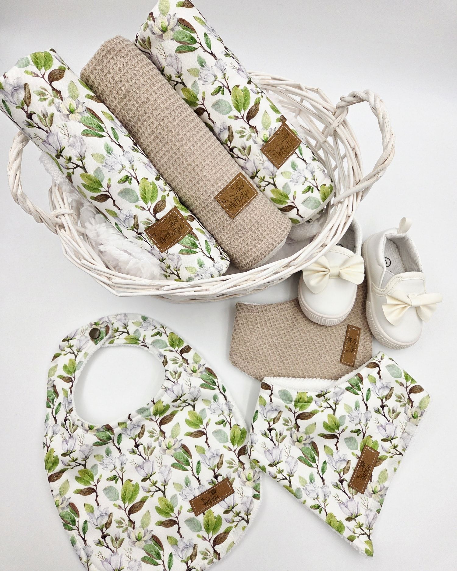 Woven basket containing beige and floral patterned baby blankets with decorative bow.