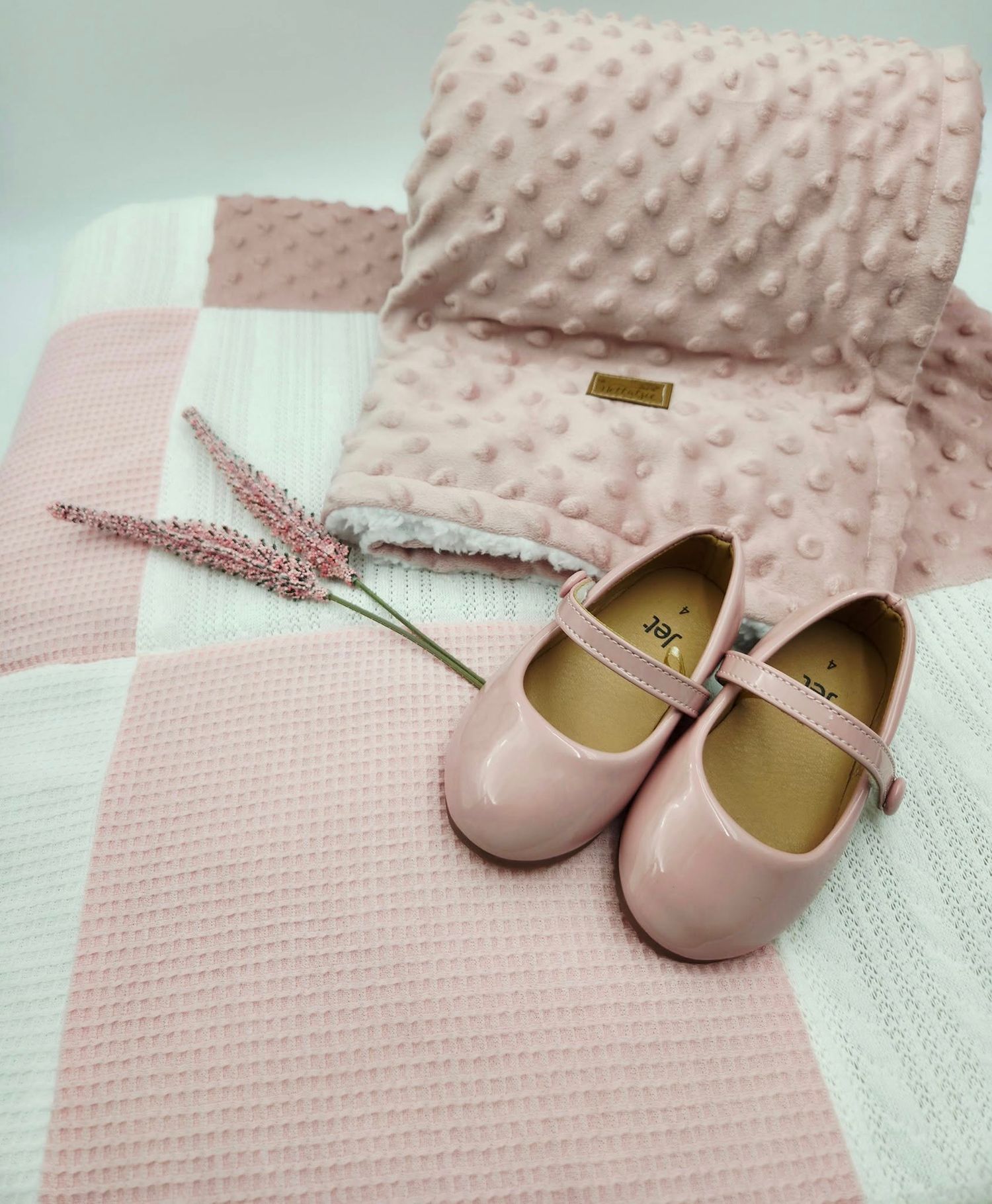 Pink textured minky blanket with matching baby shoes on mint green background.