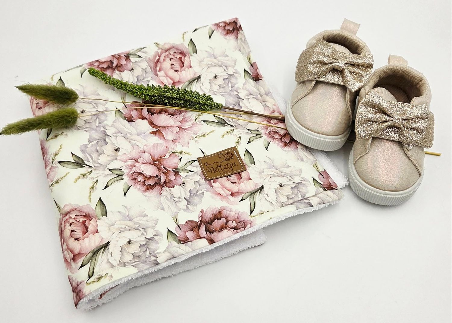 Floral baby blanket with pink roses and beige accessories arranged artistically on white background.
