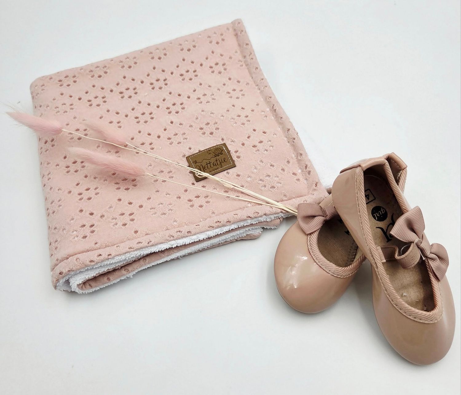 Pink eyelet fabric baby blanket paired with tan leather bow shoes on white surface.