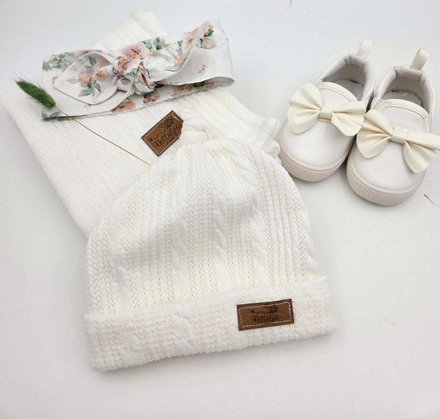 White knitted baby blanket with bow detail and matching shoes on light background.