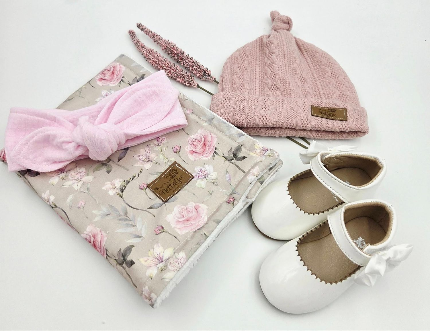 Delicate pink baby accessories including shoes, blanket and floral fabric items.