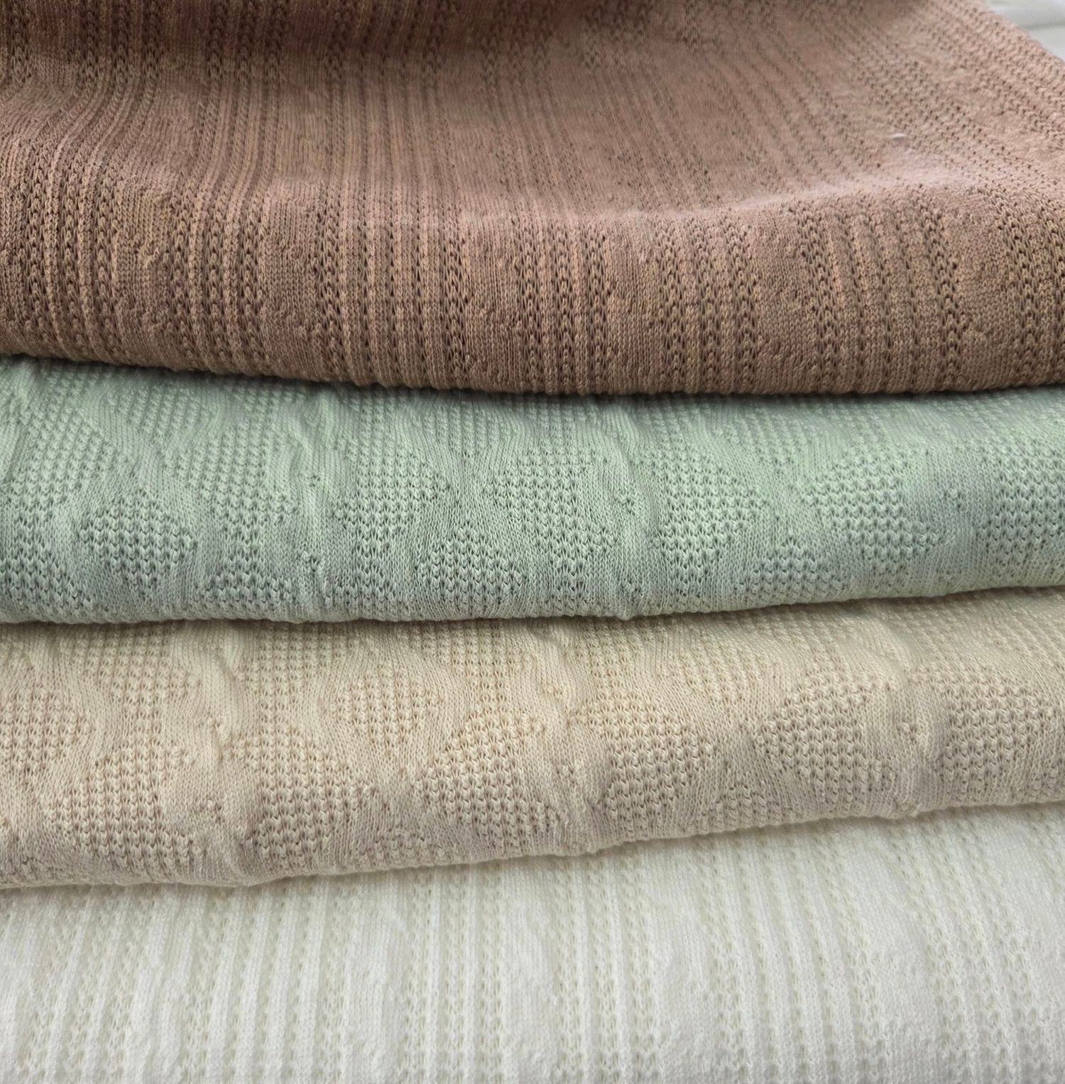 Stack of neutral knit baby blankets in varying shades of beige and mint green.