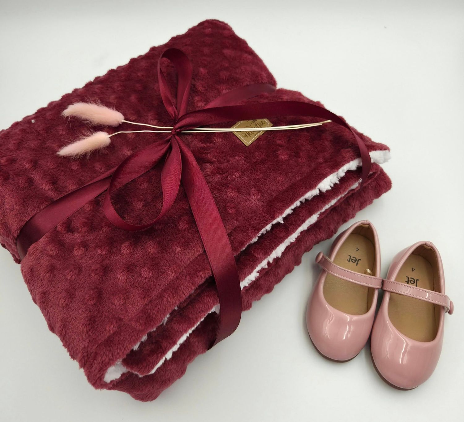 Burgundy plush blanket with pink bow and matching baby shoes displayed in sequence.