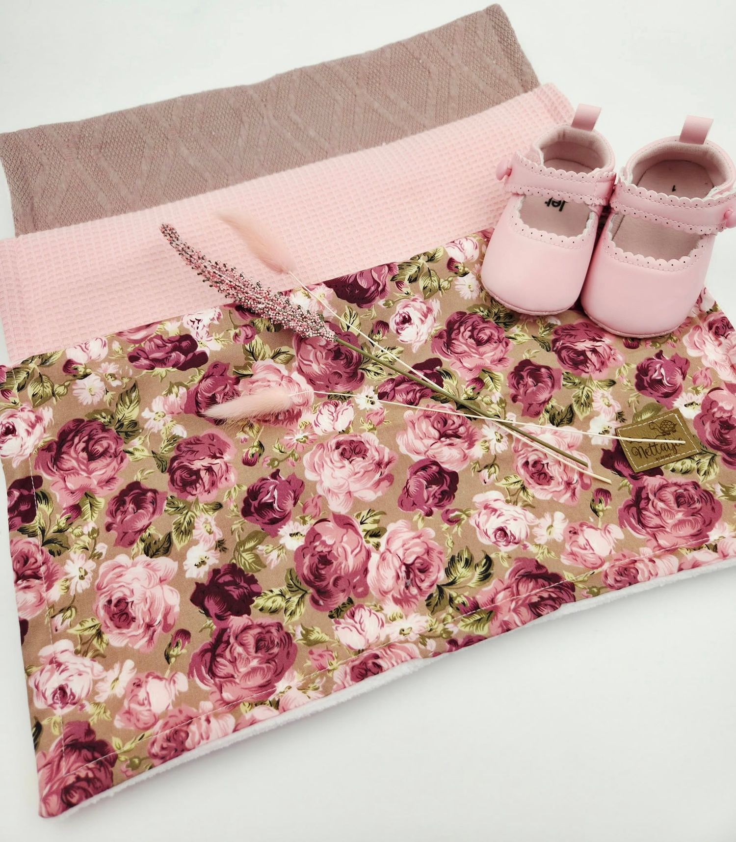 Pink floral baby blanket with matching booties displayed in a decorative arrangement.