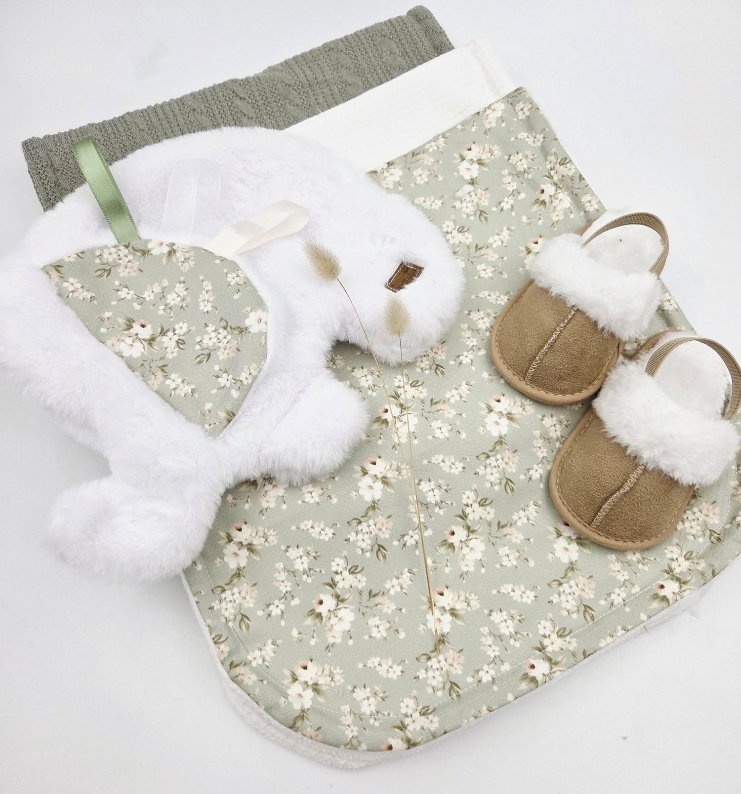 Sage green baby blanket with delicate floral pattern and white fuzzy booties.