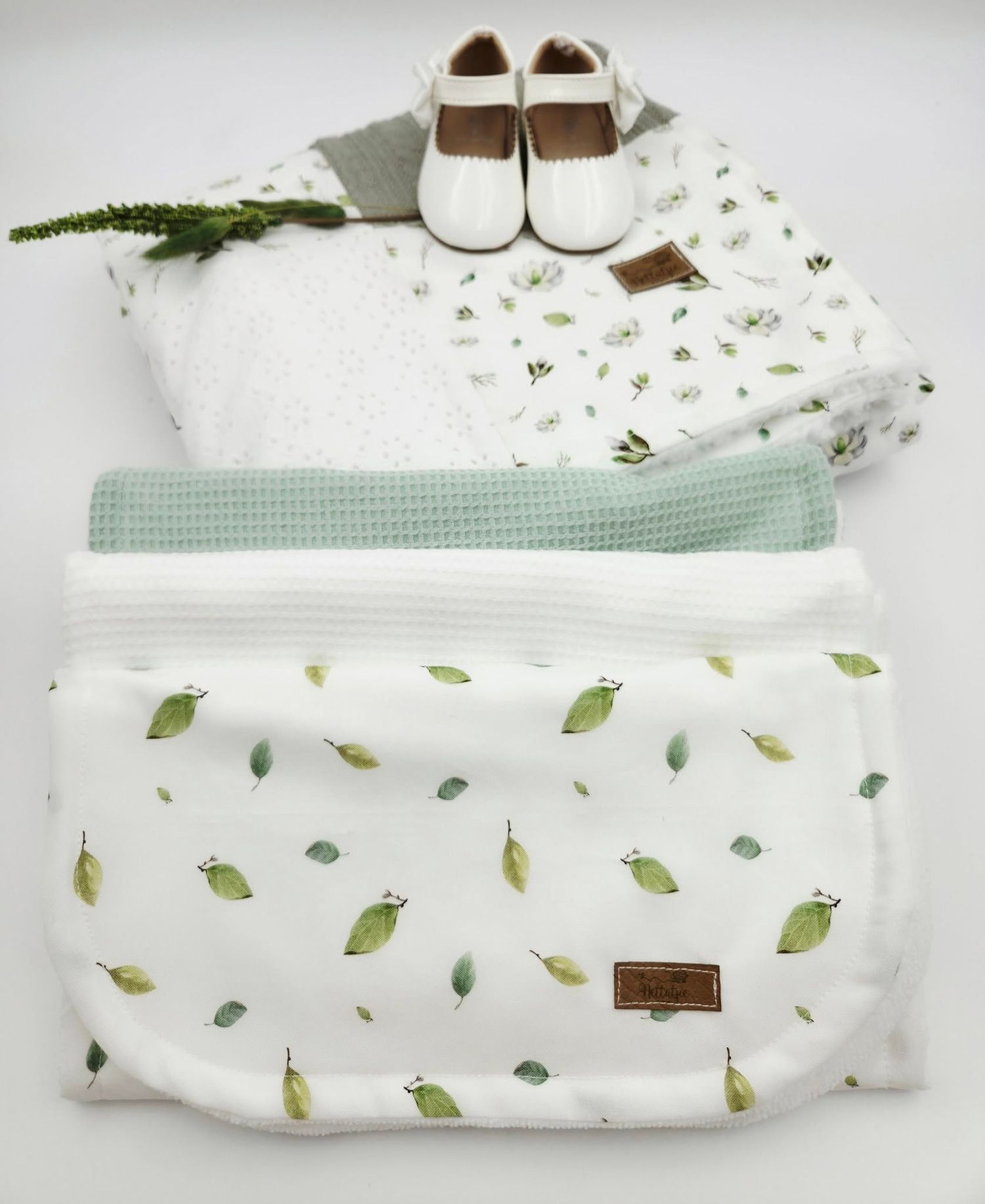 White baby blanket with green leaf pattern and matching booties tied with ribbon.