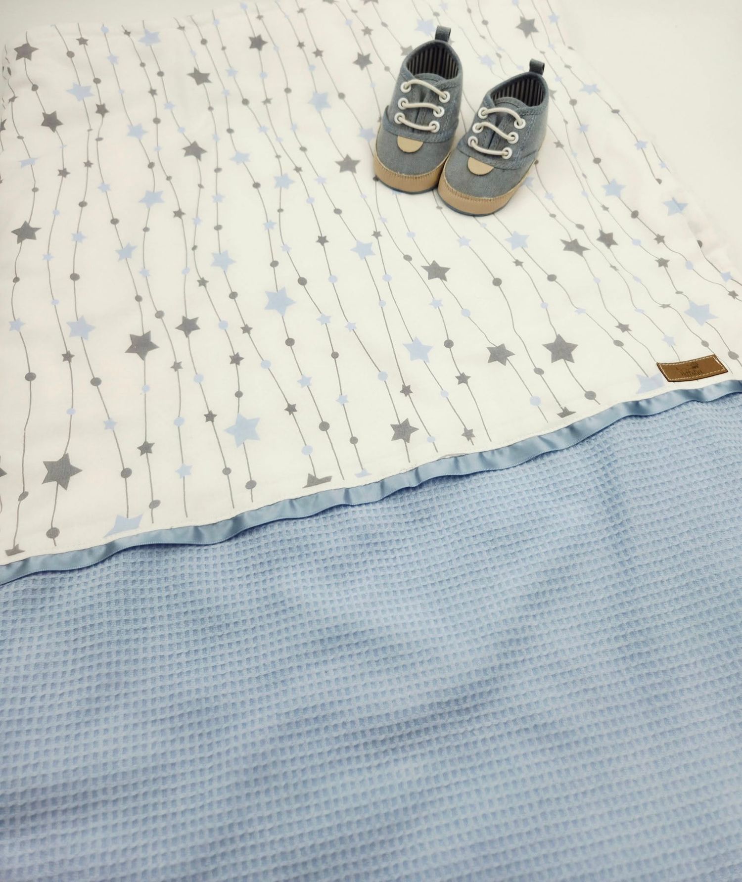 Blue waffle-textured baby blanket with star pattern and brown leather shoes.
