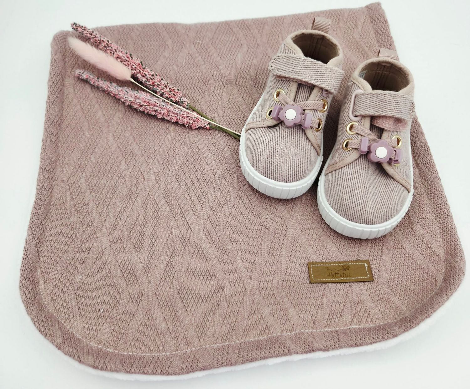 Dusty pink quilted baby blanket with small decorative shoes attached.