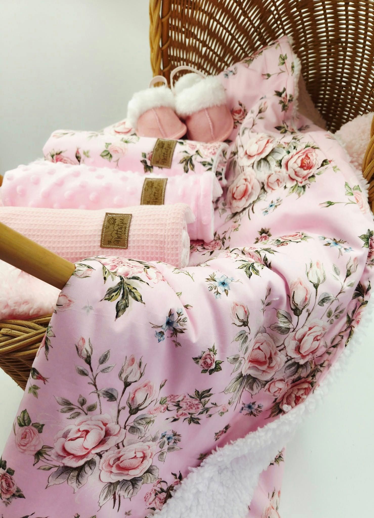 Pink floral pattern baby blanket with delicate rose print displayed on wicker furniture.