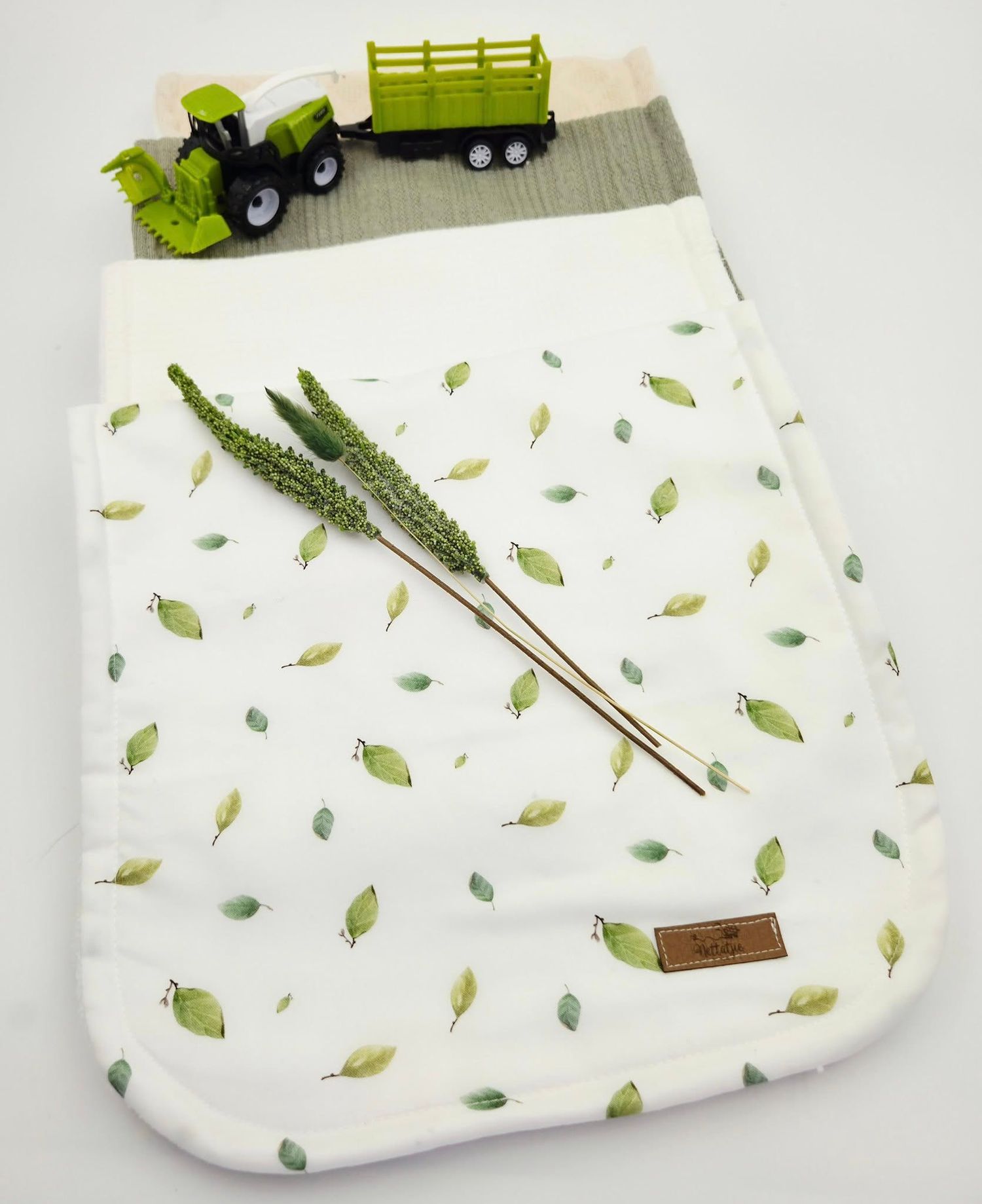 White baby blanket with scattered green leaf pattern and toy truck decoration.