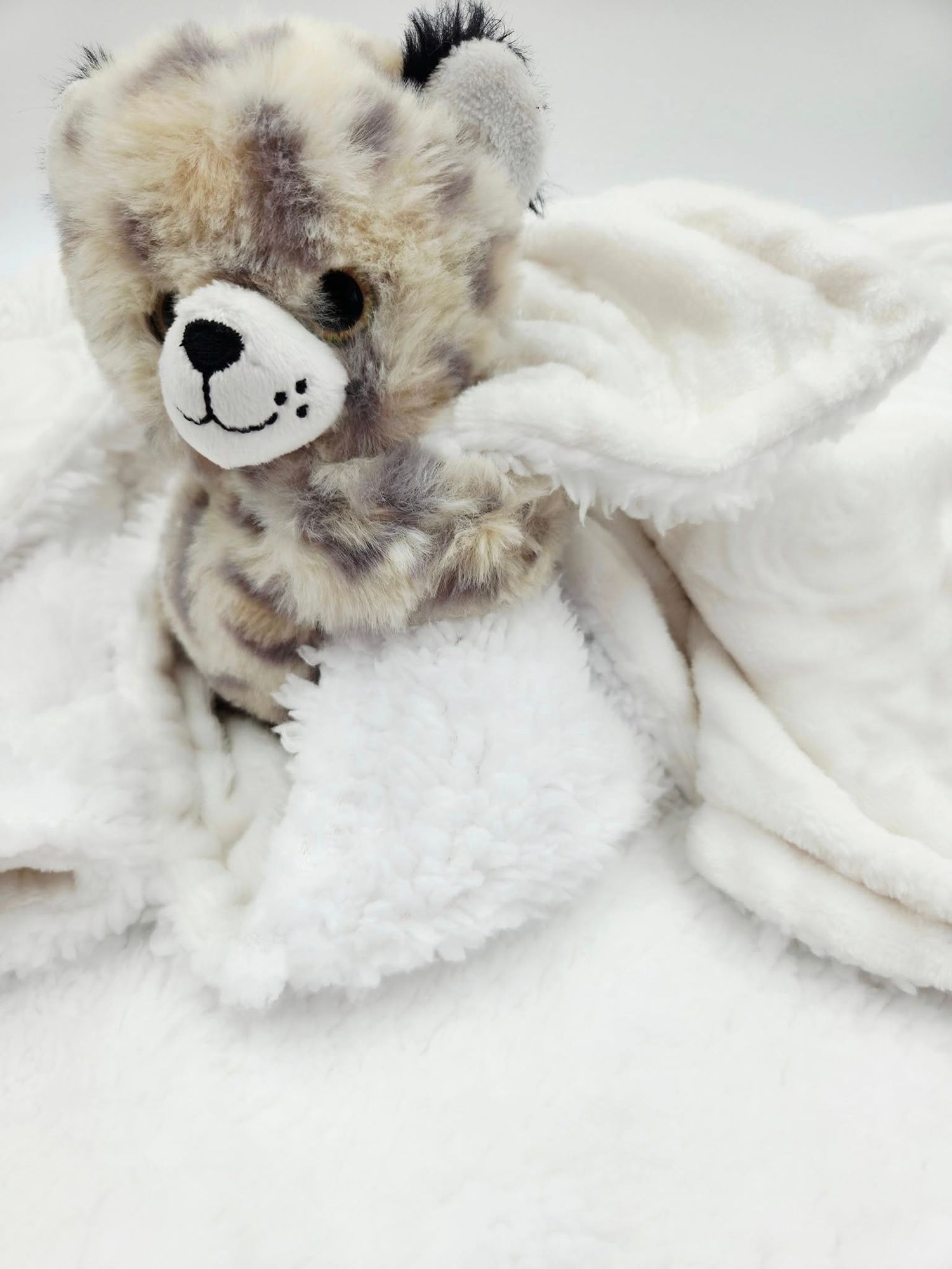 Plush teddy bear with white fluffy blanket in cozy arrangement.