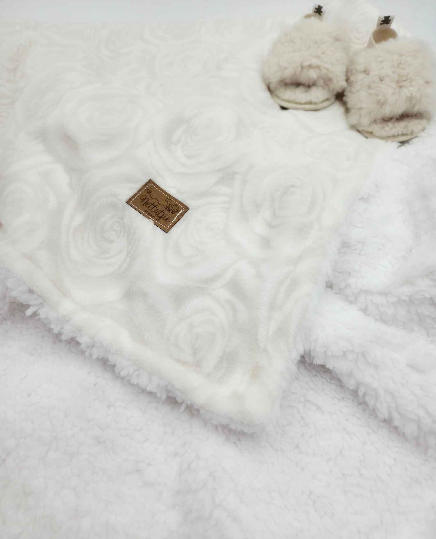 Soft white textured faux fur baby blanket with decorative tag.