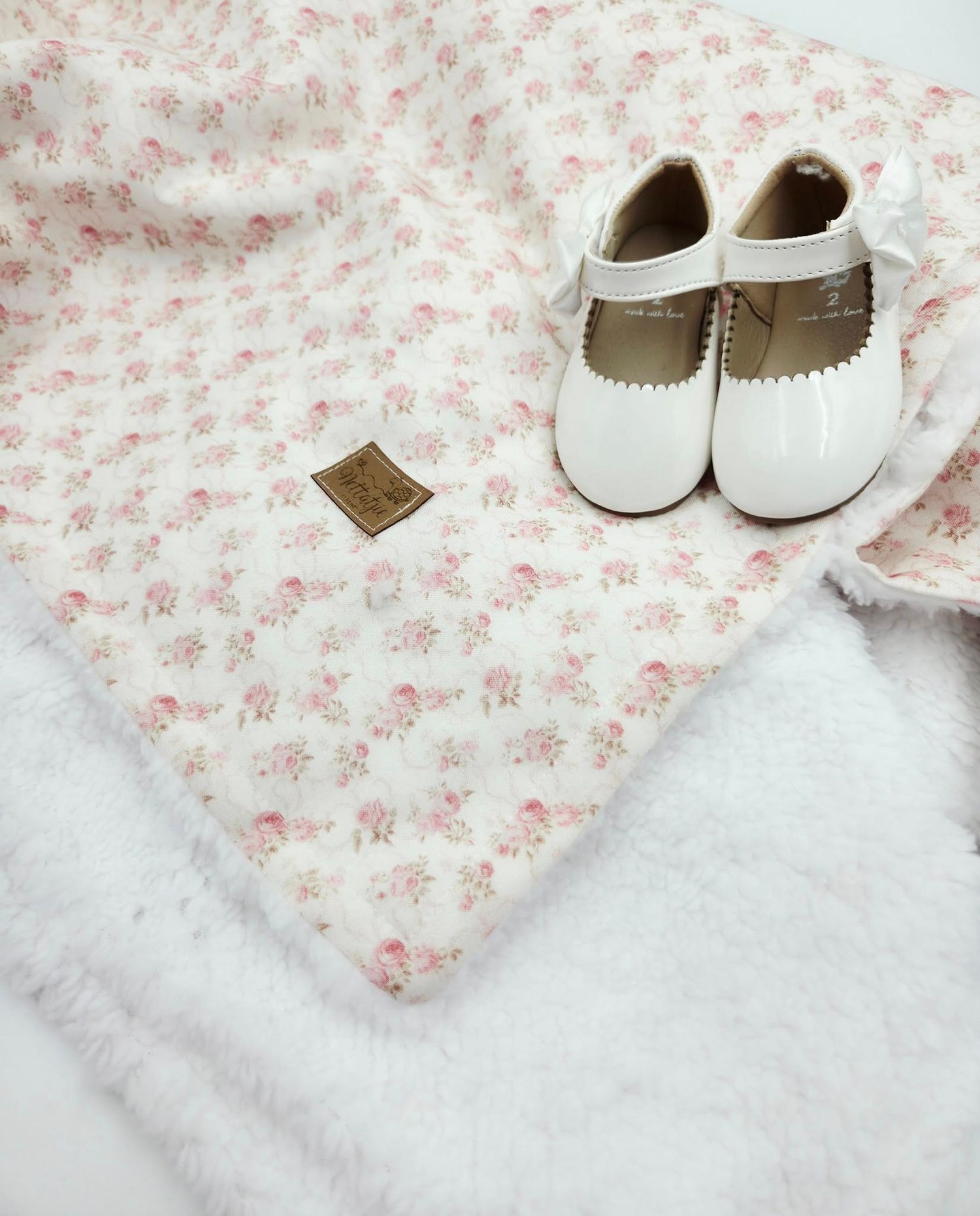 Pink floral baby blanket with white shoes and accessories in a soft, feminine arrangement.