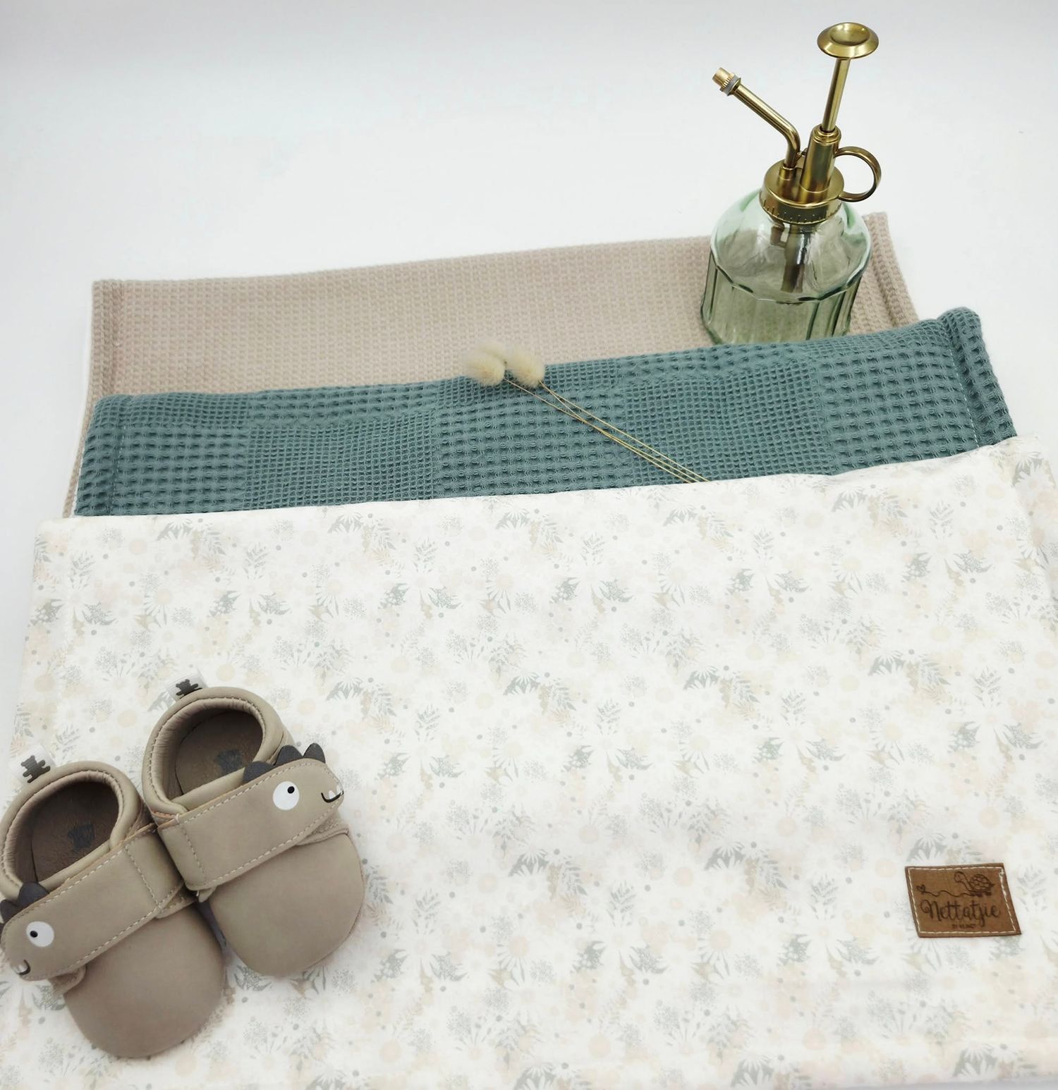 White floral baby blanket with gray baby shoes shown in various folded positions.