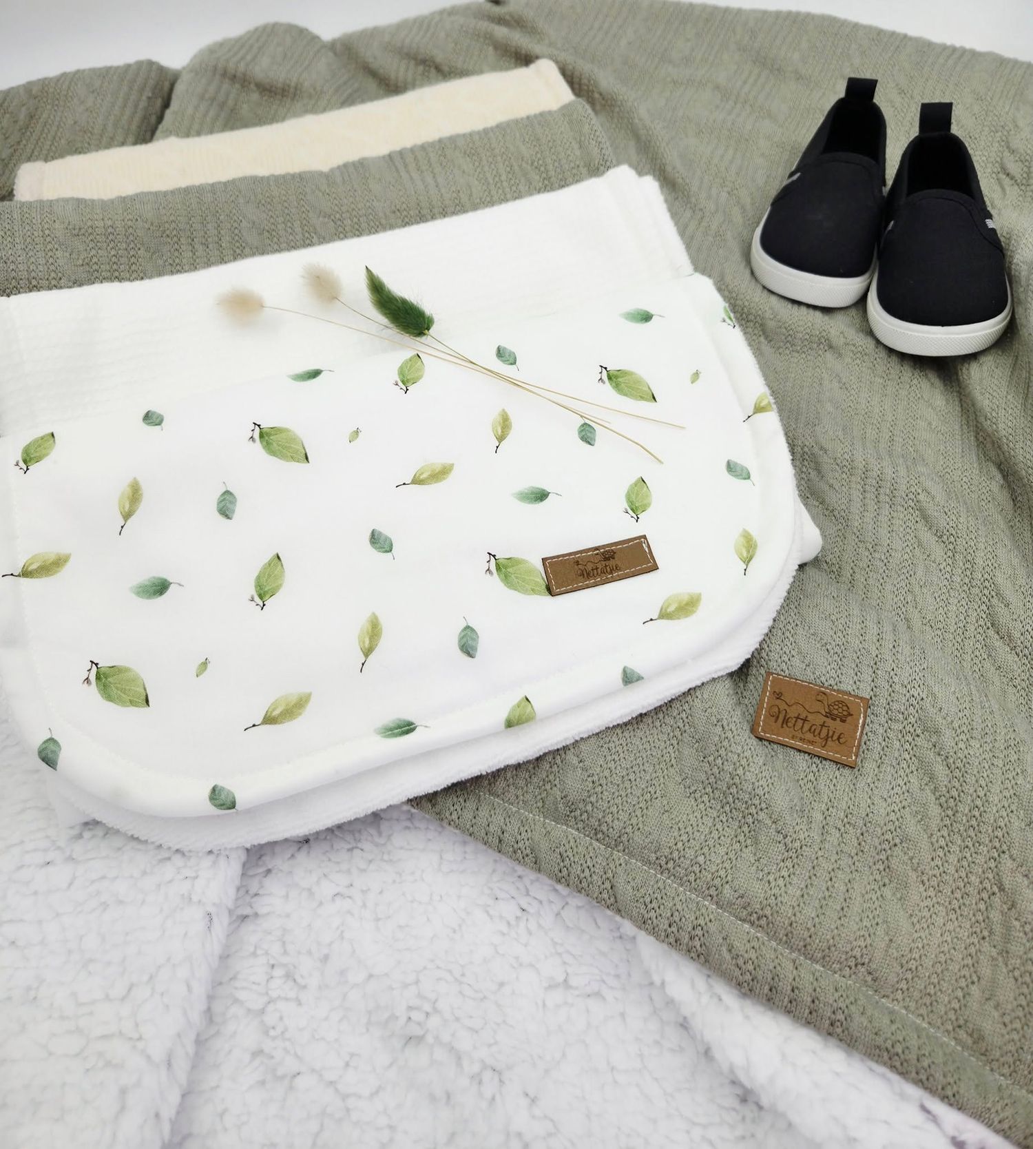 Sage green and white leaf-patterned baby blanket with black shoes displayed on marble surface.