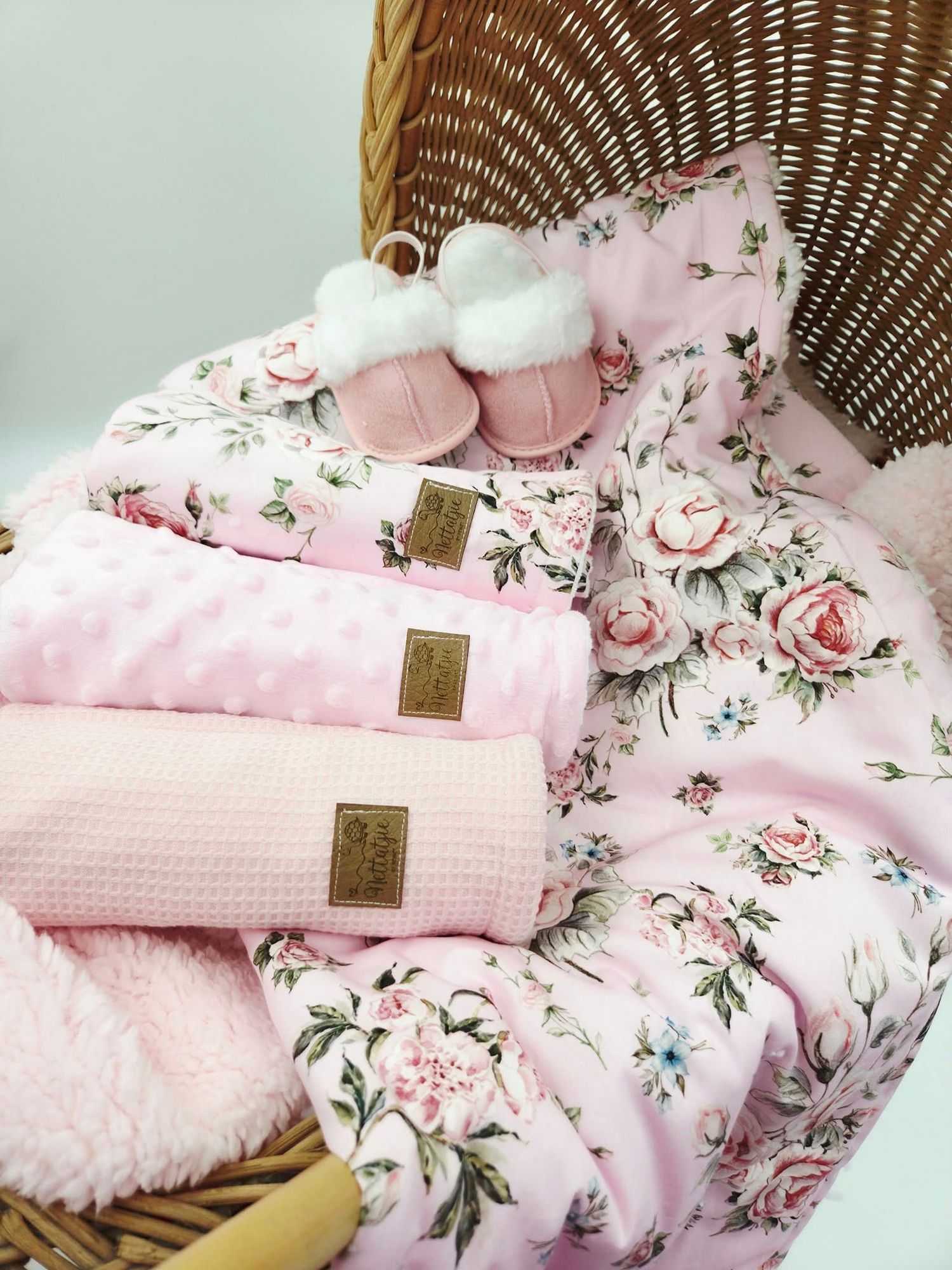 Pink floral baby blanket and accessories arranged in wicker basket with soft textures.