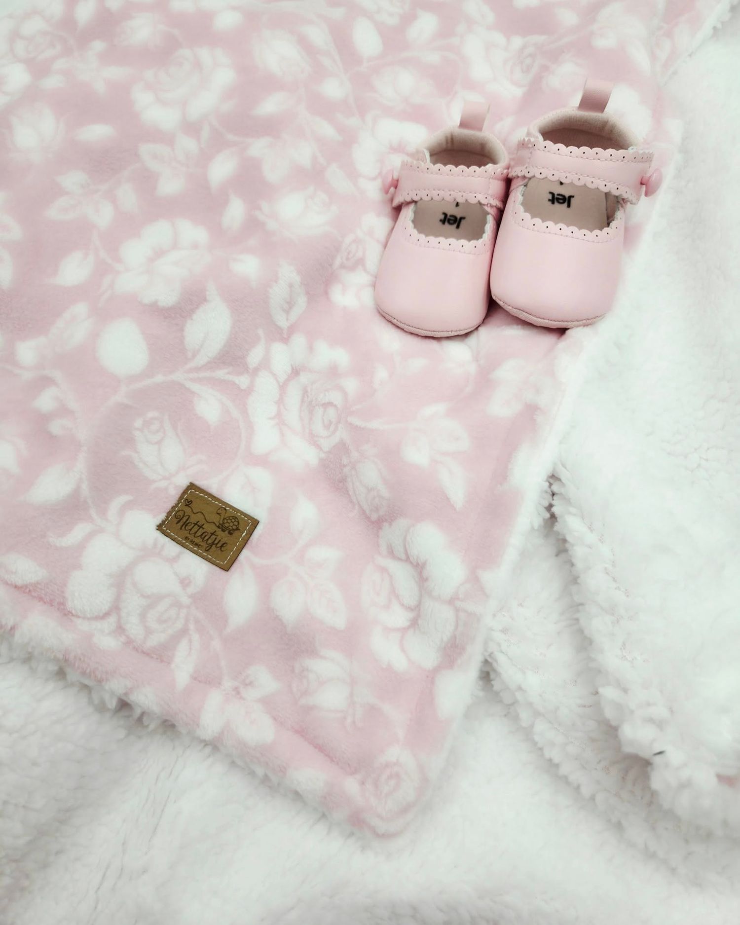 Pink floral baby blanket with small pink leather shoes and gold label.