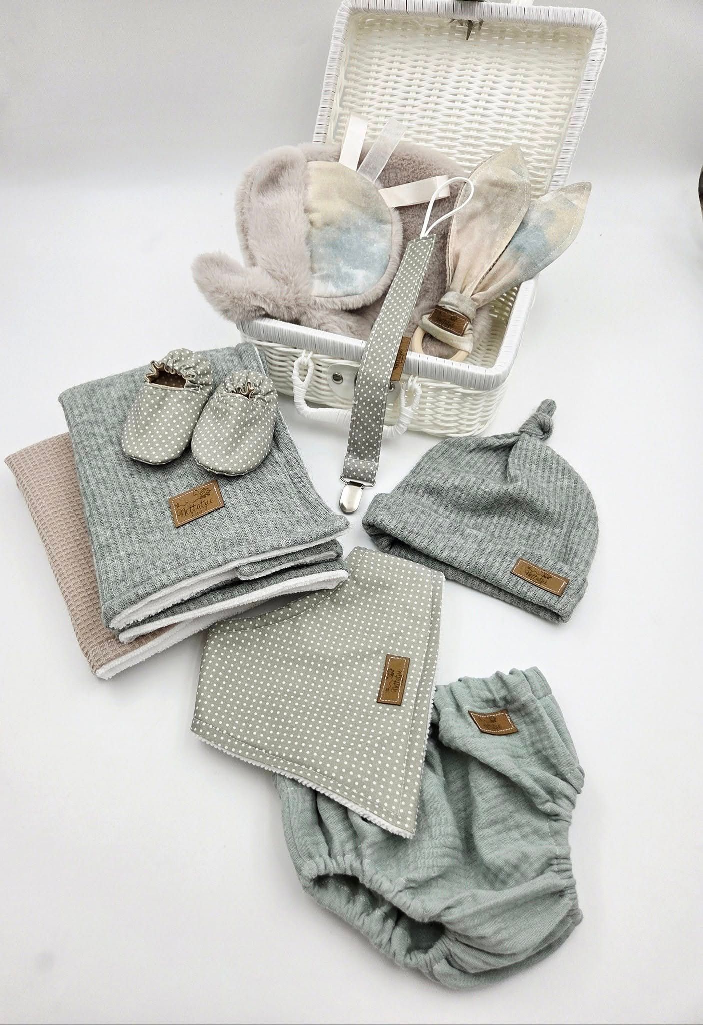 White wicker basket filled with gray baby accessories including blankets, hats and clothing.