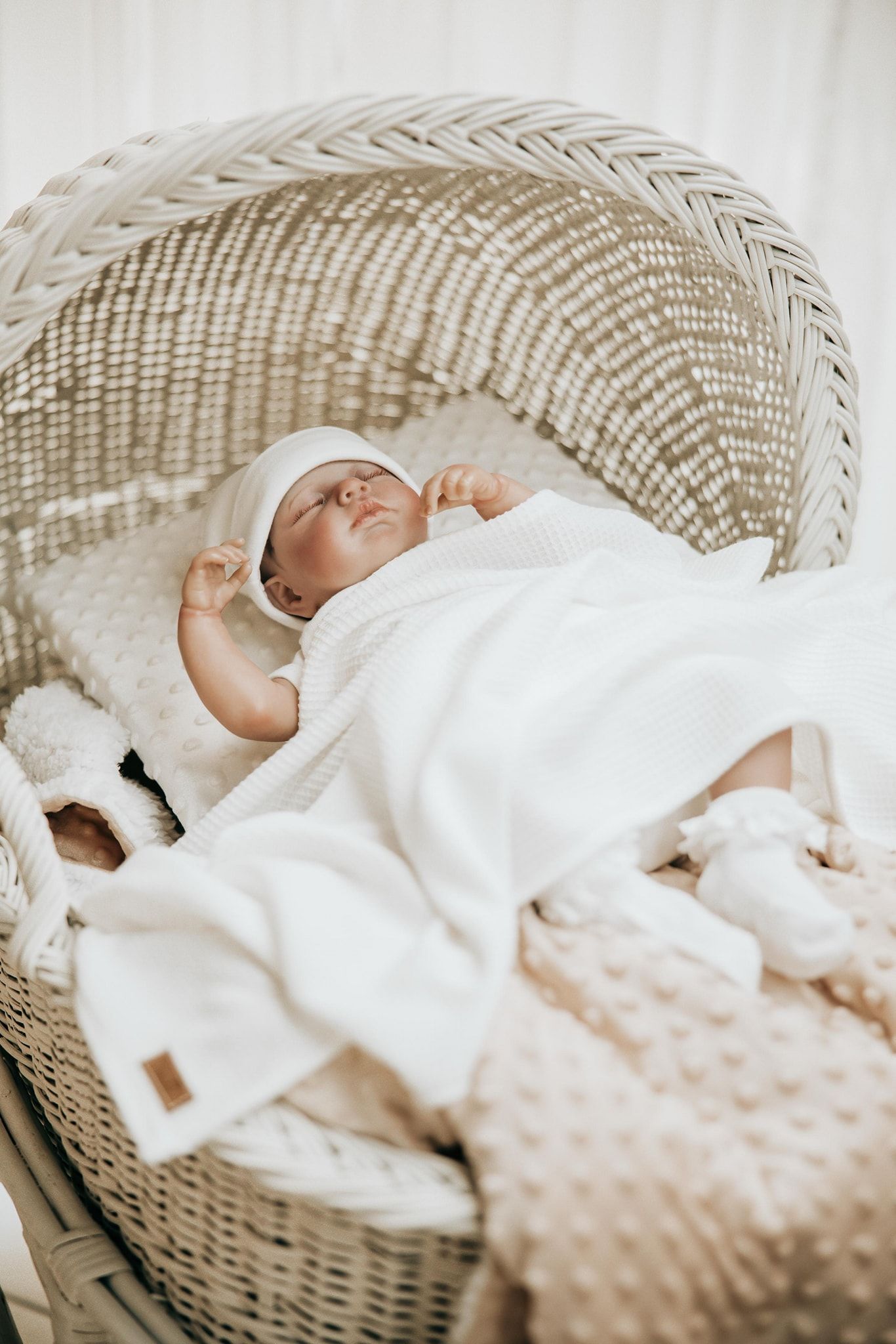 A sleeping baby wrapped in white blankets rests peacefully in a woven wicker basket.