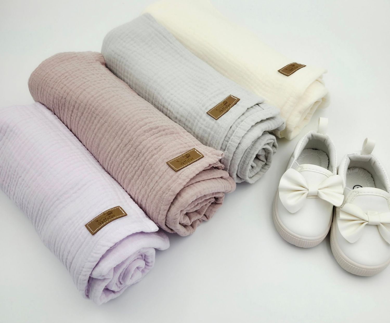 Soft pastel baby blankets and white bow shoes arranged on a neutral surface.