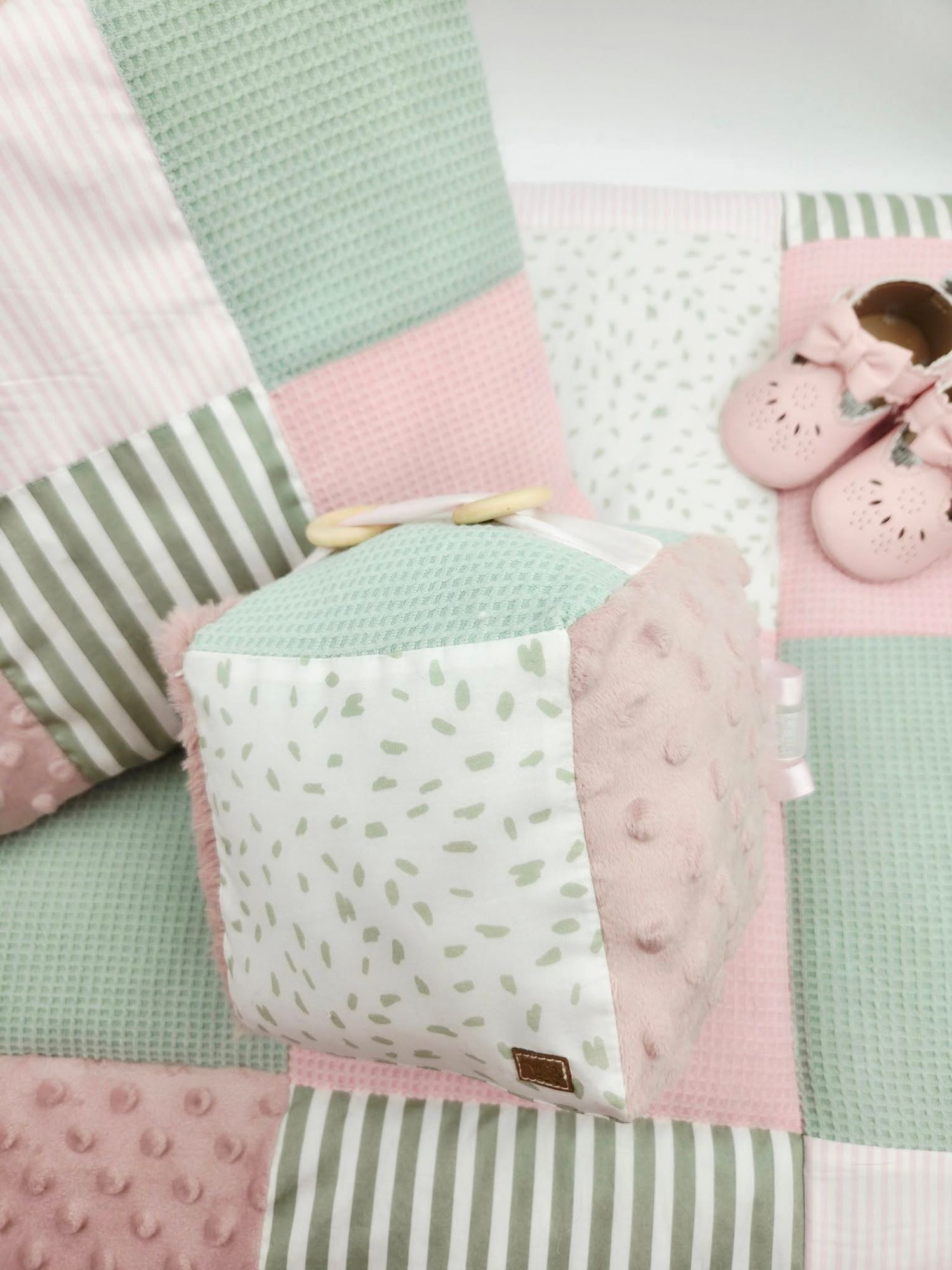 Close-up of mint green and pink patchwork baby blanket with textured dots and stripes.
