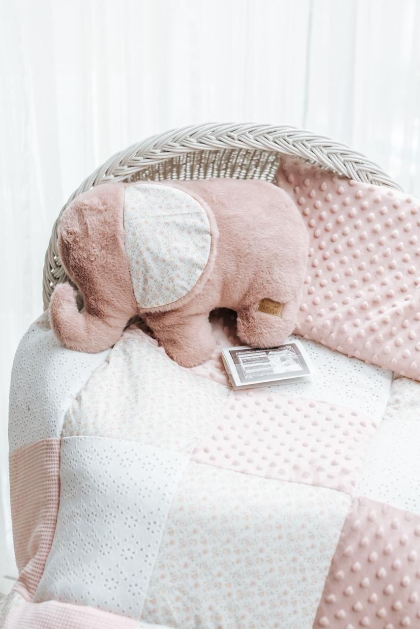 Pink plush elephant toy resting on white and pink textured blankets with ultrasound photos.