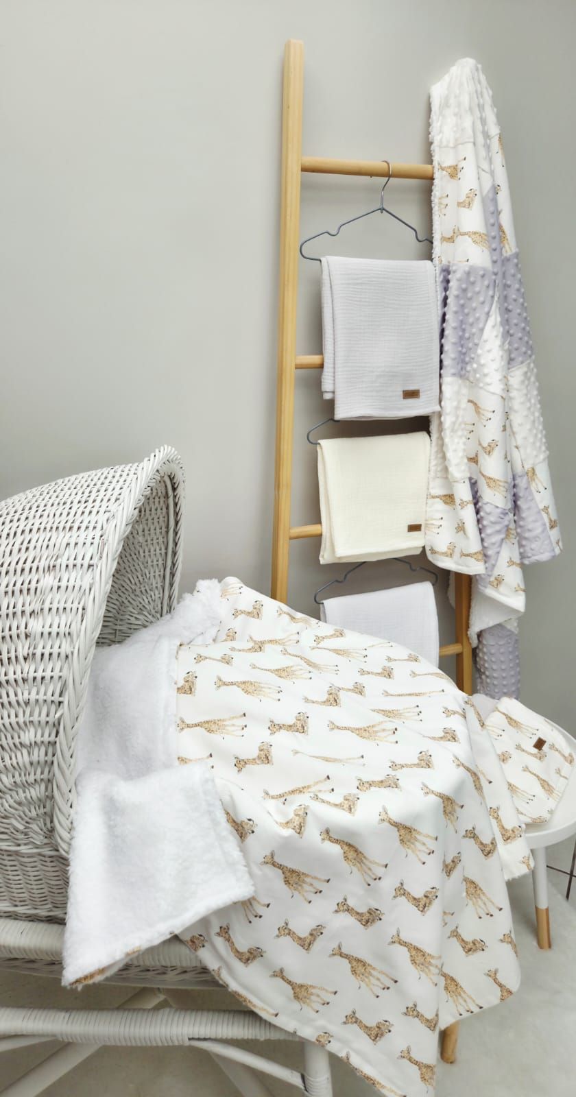 Cozy nursery corner with giraffe print blanket, wooden ladder towel rack, and white wicker chair.