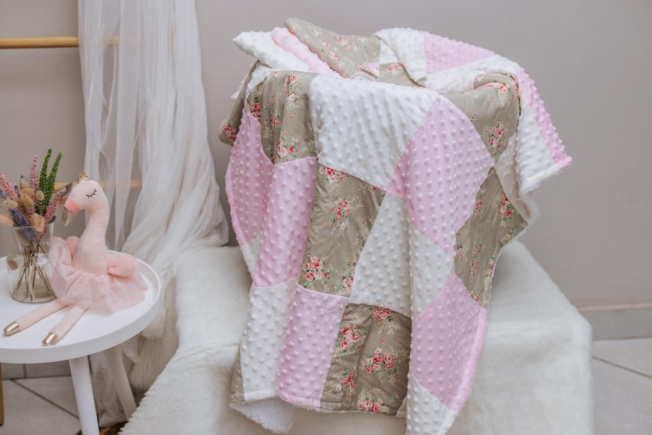 Pink and brown floral patchwork baby blanket displayed with coordinating nursery decor items on white furniture.