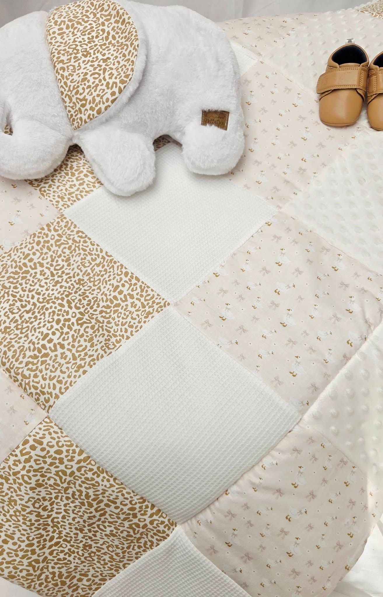 Neutral toned patchwork baby quilt with leopard print and white minky squares, paired with a plush elephant toy and tan leather baby shoes.