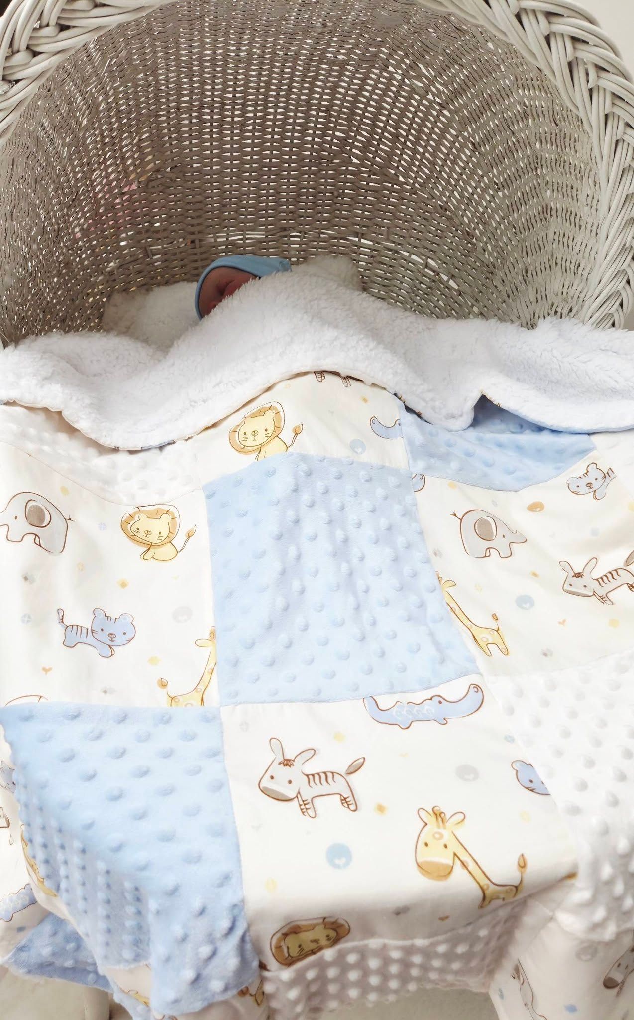 Baby sleeping in wicker Moses basket with blue minky dot patchwork blanket featuring cute safari animals.