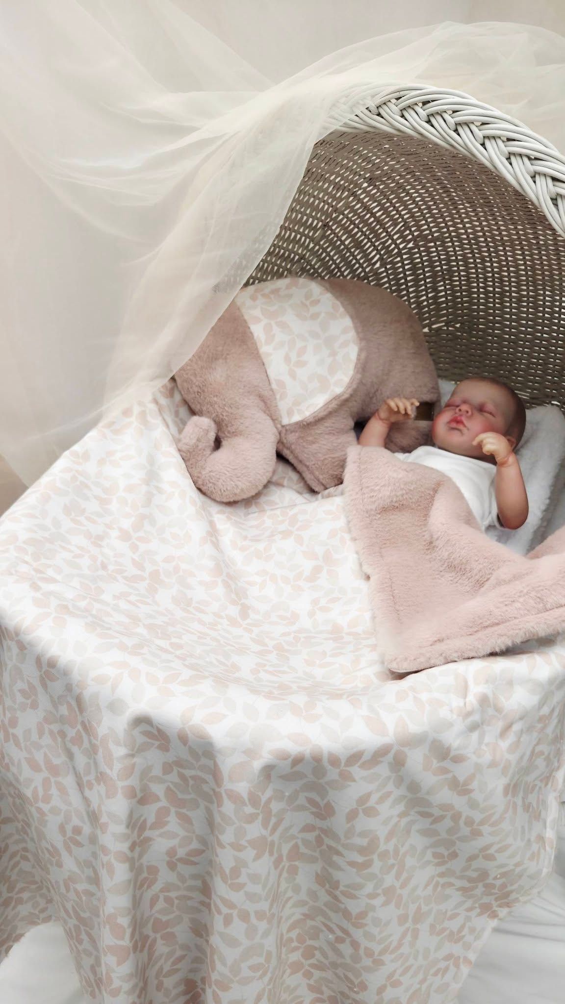 Newborn baby sleeping peacefully in a wicker Moses basket with pink blanket and elephant stuffed animal toy.