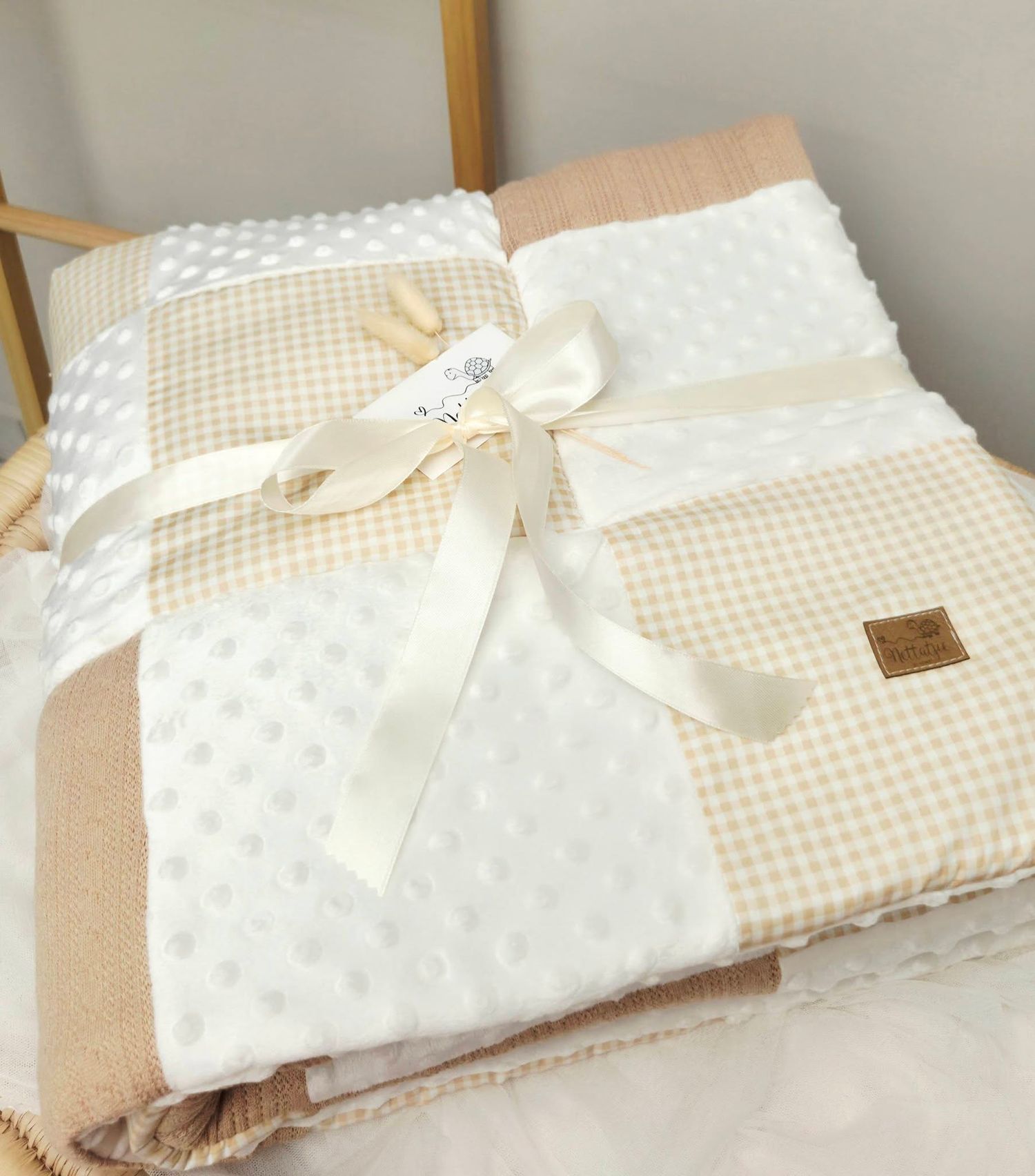 Soft beige and white baby blanket set with dotted texture, gingham pattern, tied with a satin ribbon bow.