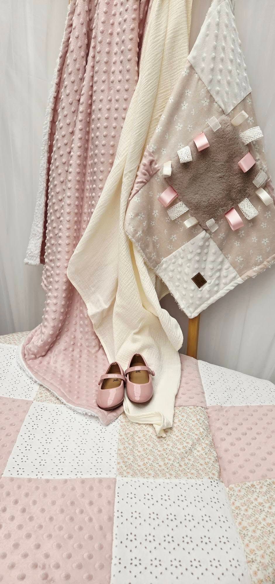 Pink and cream baby blankets with textured minky fabric displayed with small pink Mary Jane shoes on a patchwork quilt.