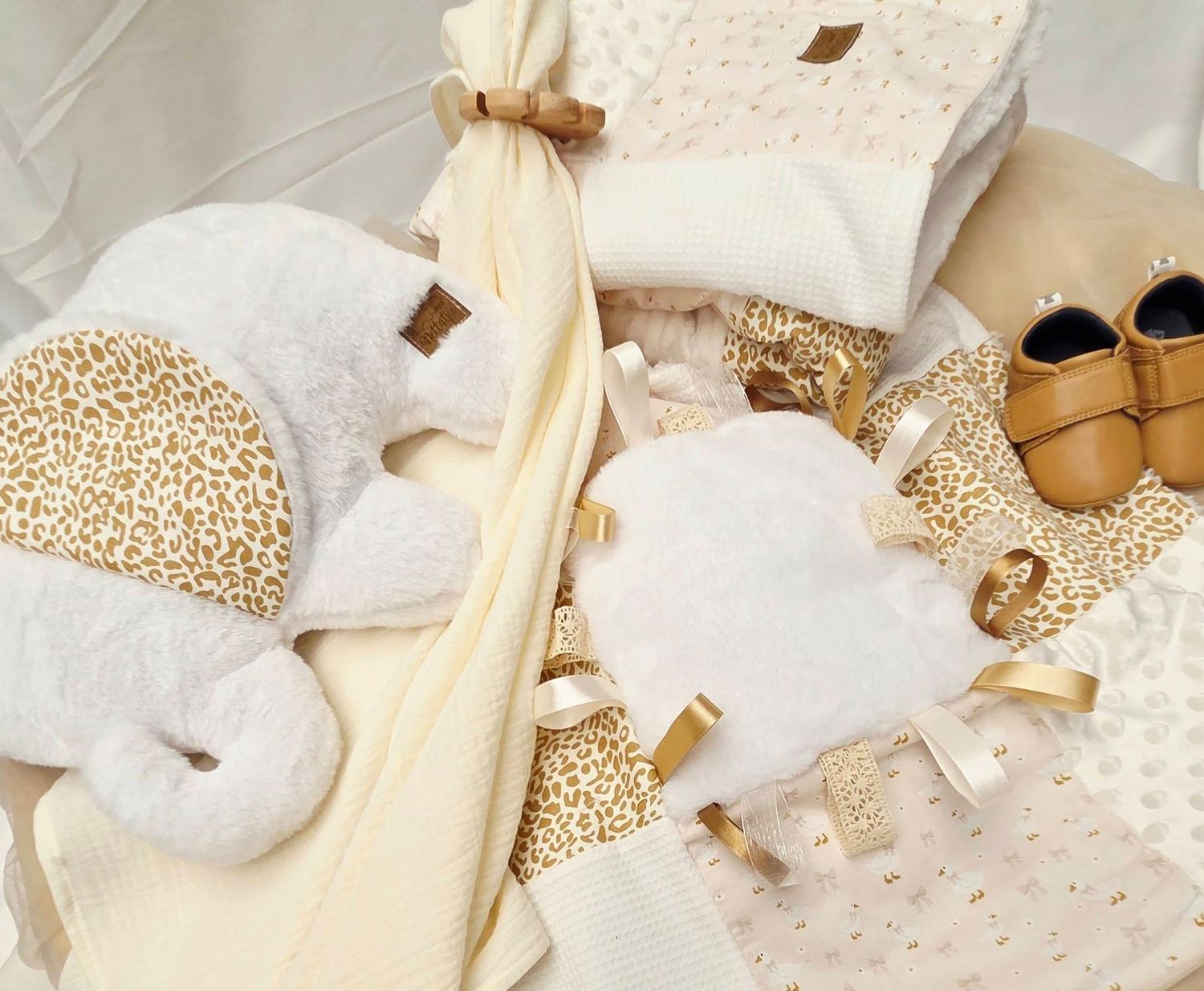 Luxury baby gift set with cream and gold leopard print items including blankets, hats, shoes, and accessories.