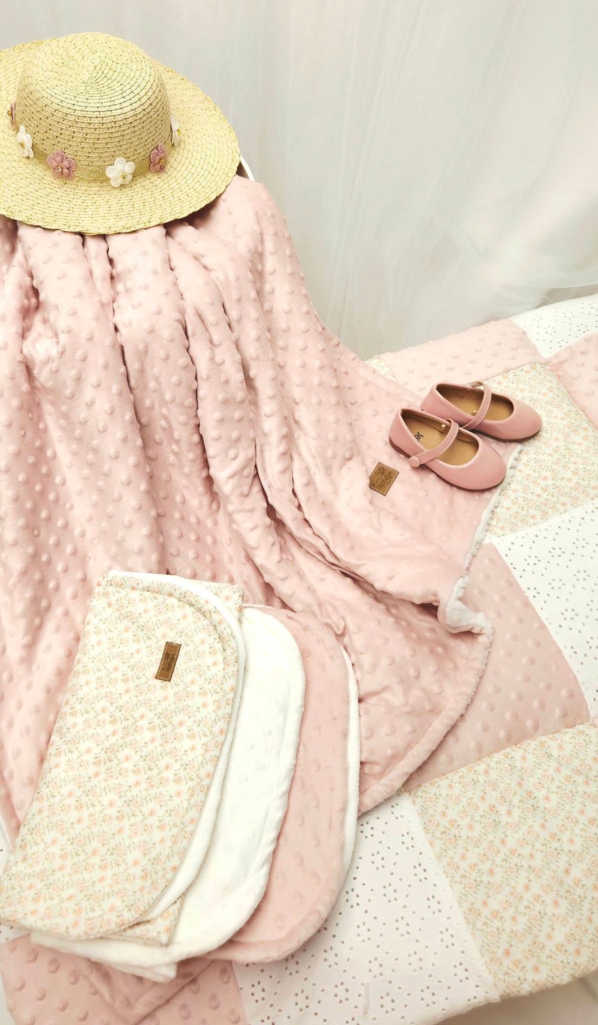 Pink baby girl set with textured blanket, straw hat with flowers, Mary Jane shoes, and white quilted changing pad.