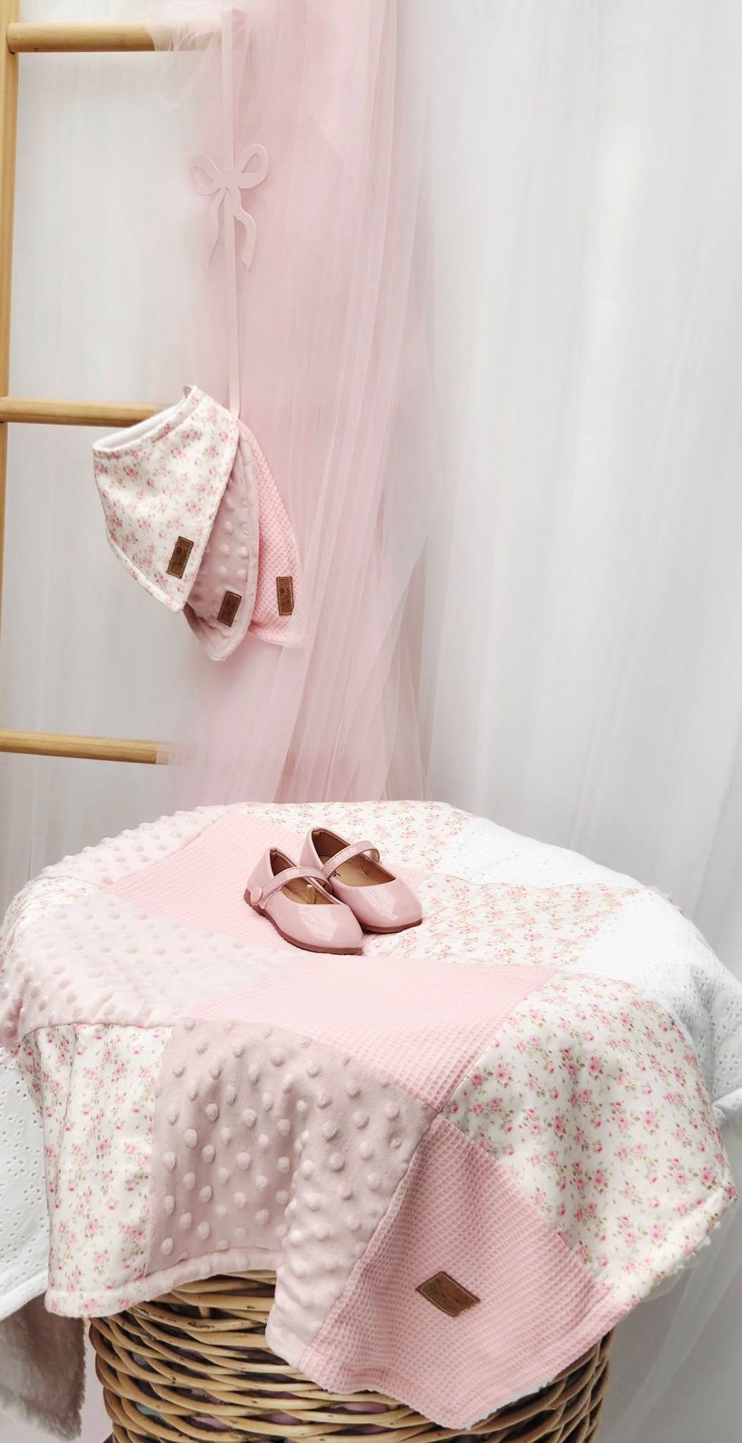 Pink baby girl gift set with floral blanket, bonnet, and Mary Jane shoes displayed on wicker basket.