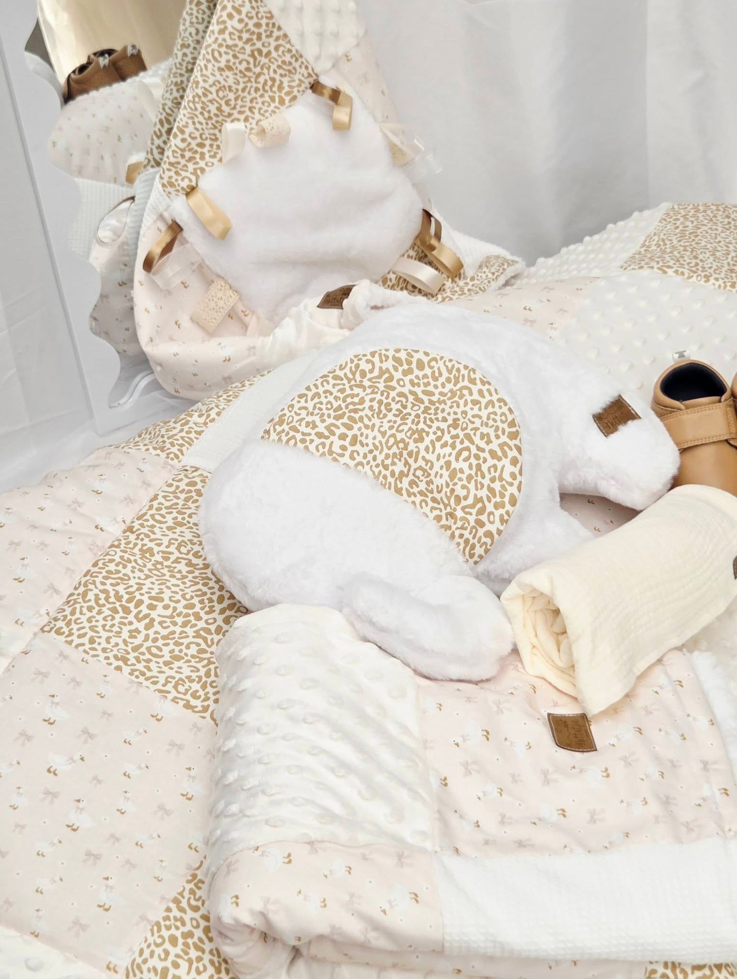 Soft baby bedding set in cream and gold leopard print with plush white blanket, pillow, and accessories.
