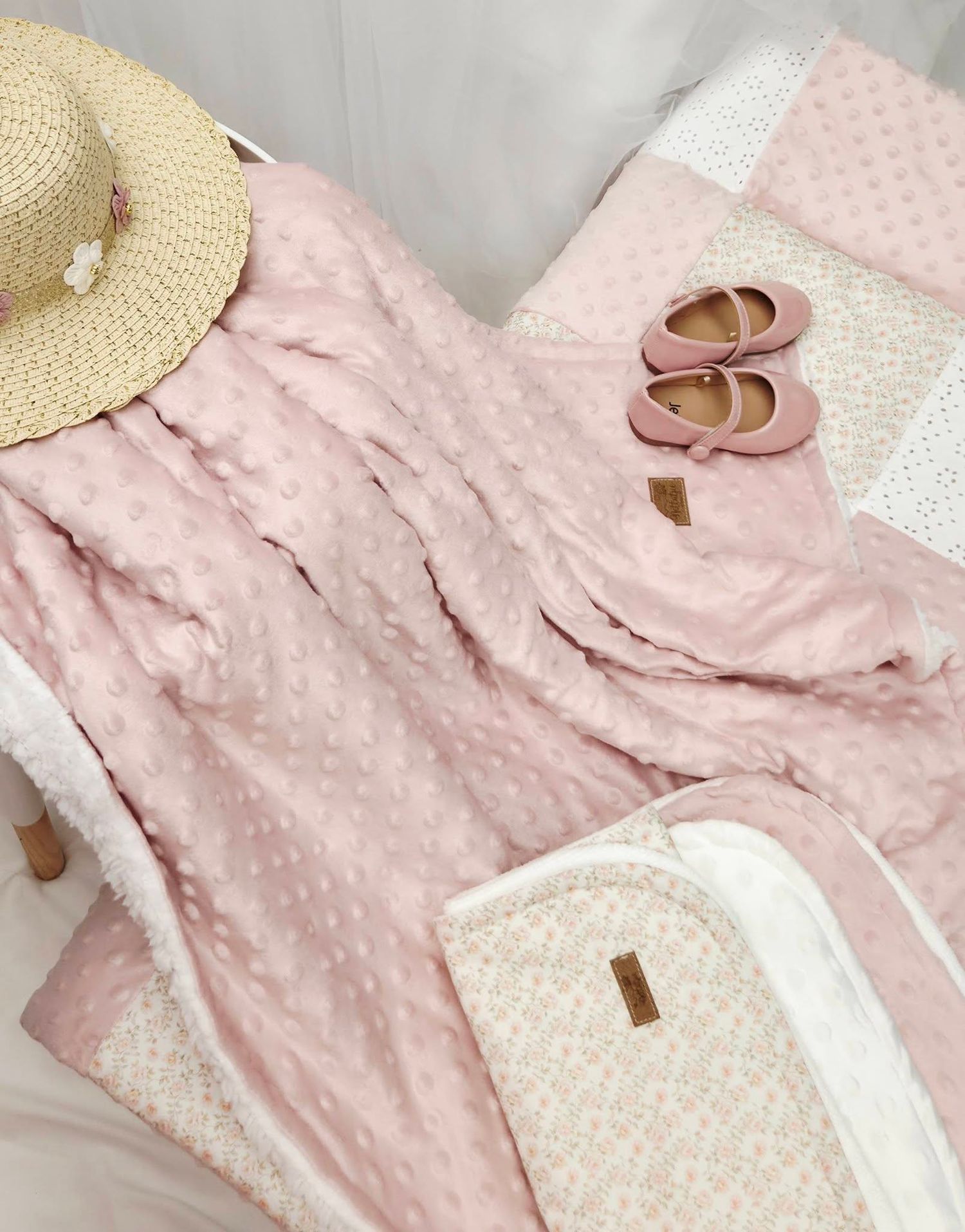 Pink minky baby blanket with sherpa trim, displayed with a straw hat and pink Mary Jane shoes on white bedding.