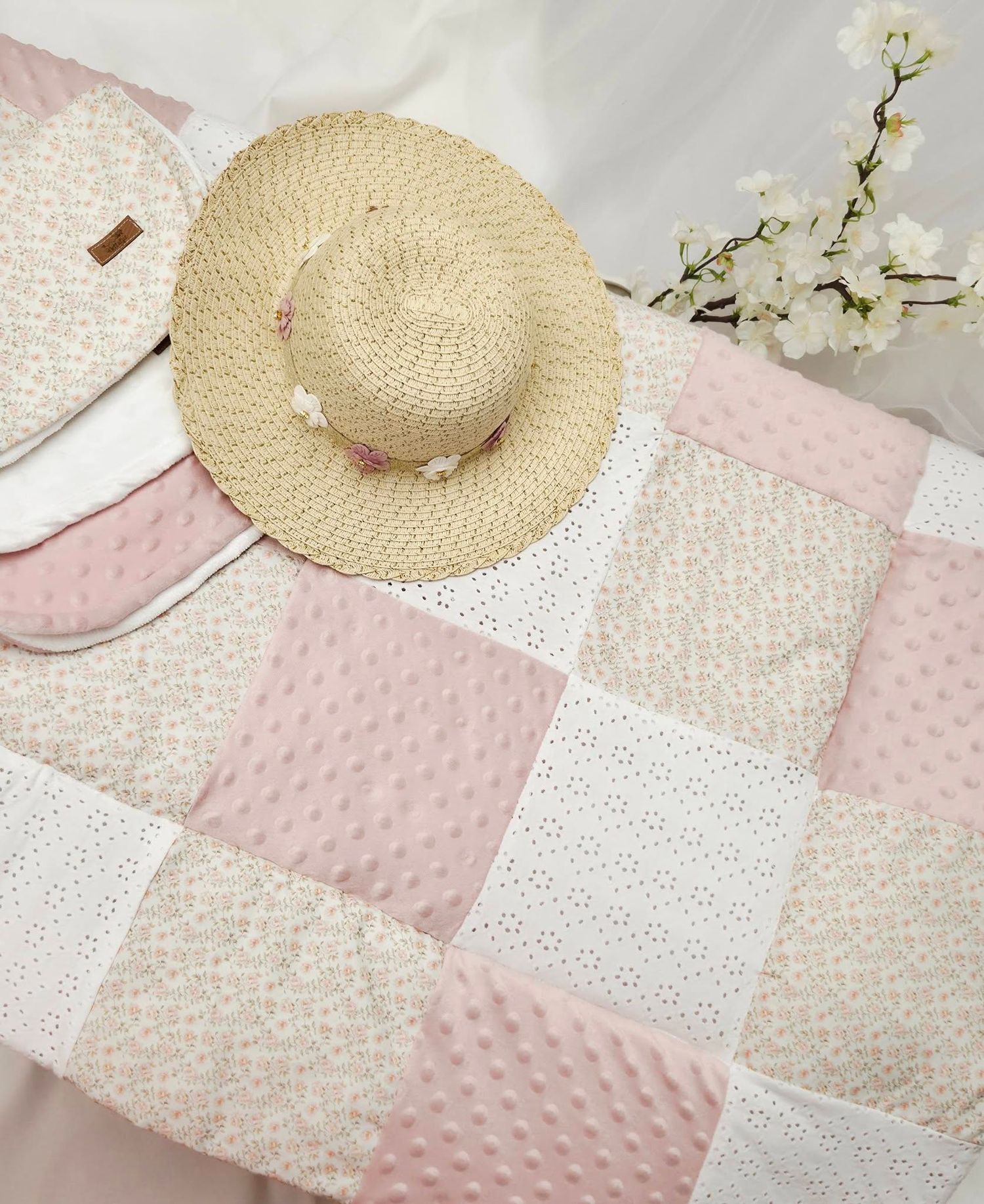 Pink and cream patchwork quilt with straw hat and white cherry blossoms, perfect for a baby girl nursery decor.