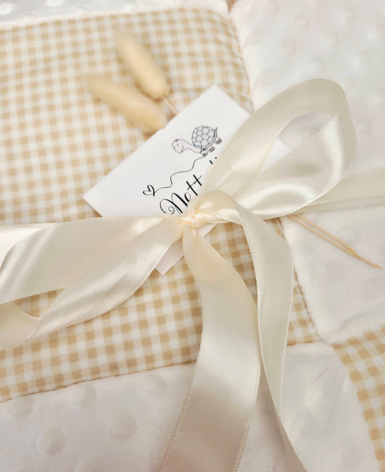 Elegant gift wrapped in beige gingham and polka dot fabric, tied with a cream satin ribbon bow and gift tag.