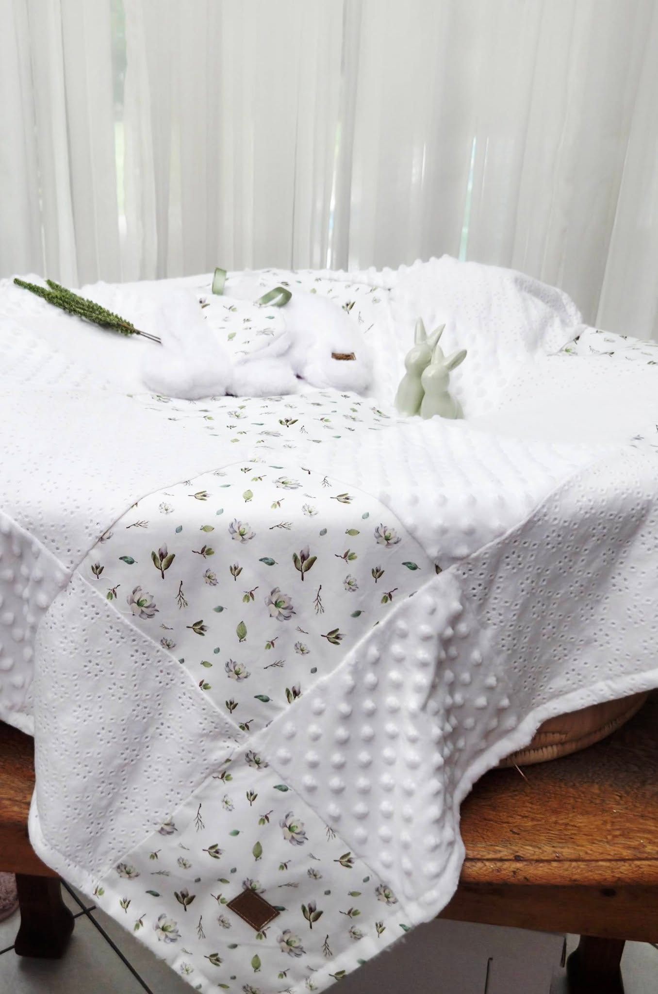White minky dot baby blanket with floral print fabric, displayed on a wooden bench with bunny toys and greenery.