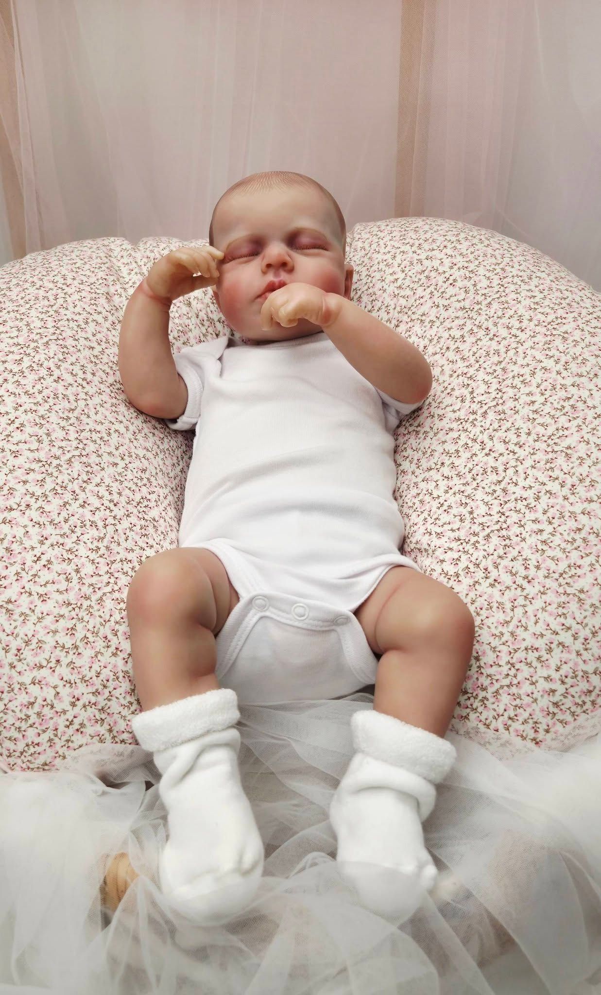 Peaceful newborn baby in white onesie and socks sleeping on a floral nursing pillow with hands near face.